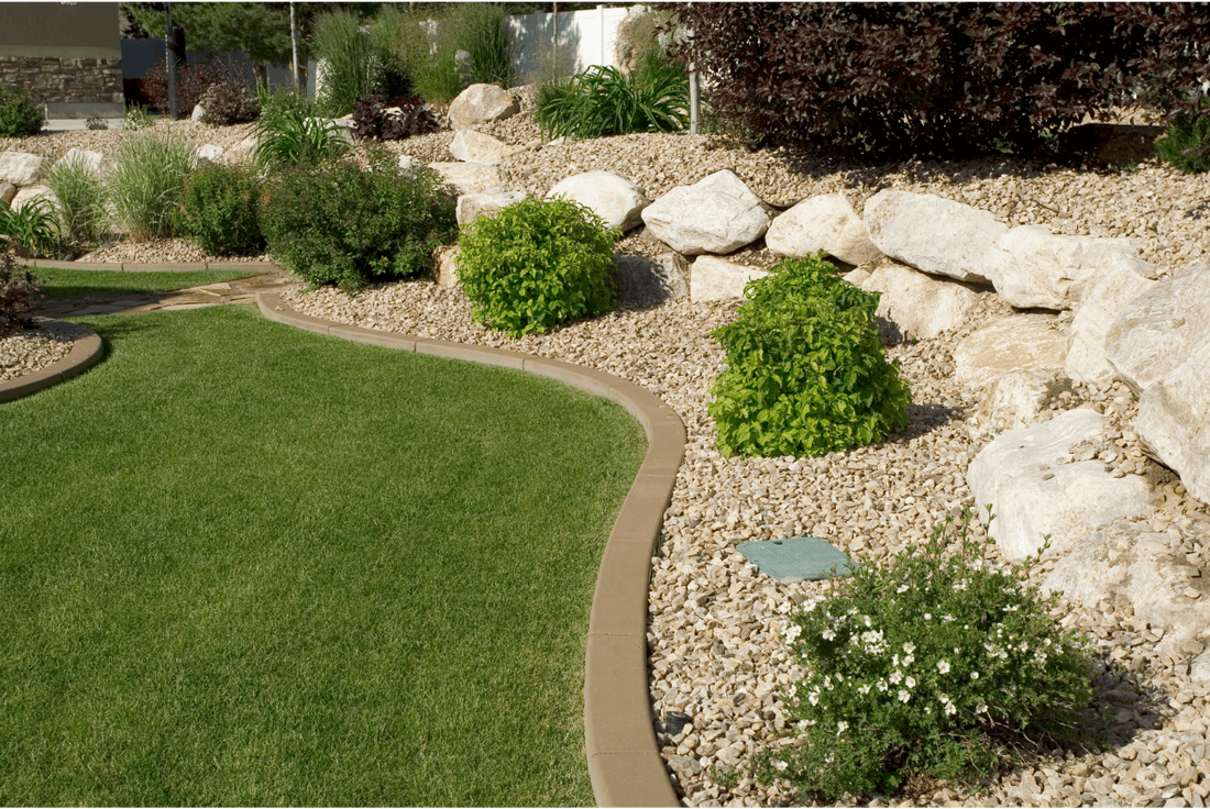 Manicured flower bed with large rocks, green shrubs and a concrete border